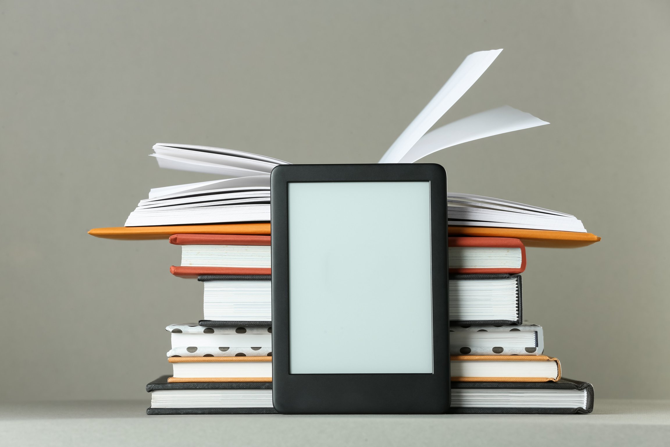 Modern E-Book Reader and Stack of Hard Cover Books on Light Grey